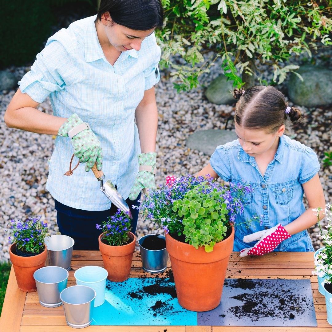 Woman and young girl gardening together, planting flowers in pots outdoors.