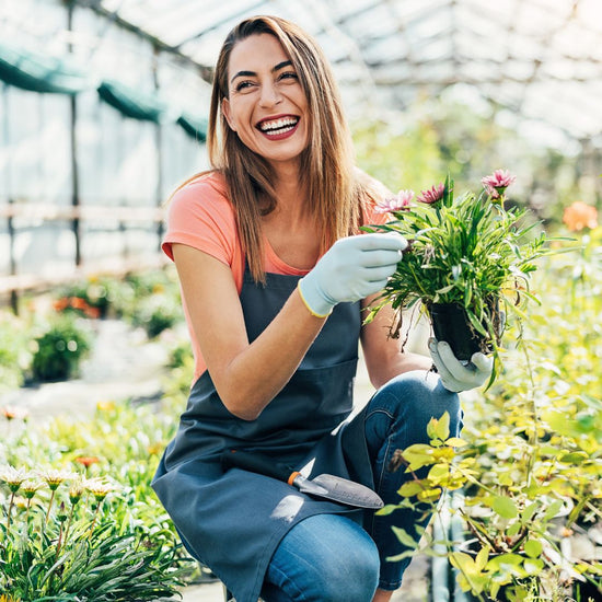 Woman in a greenhouse holding a plant and smiling